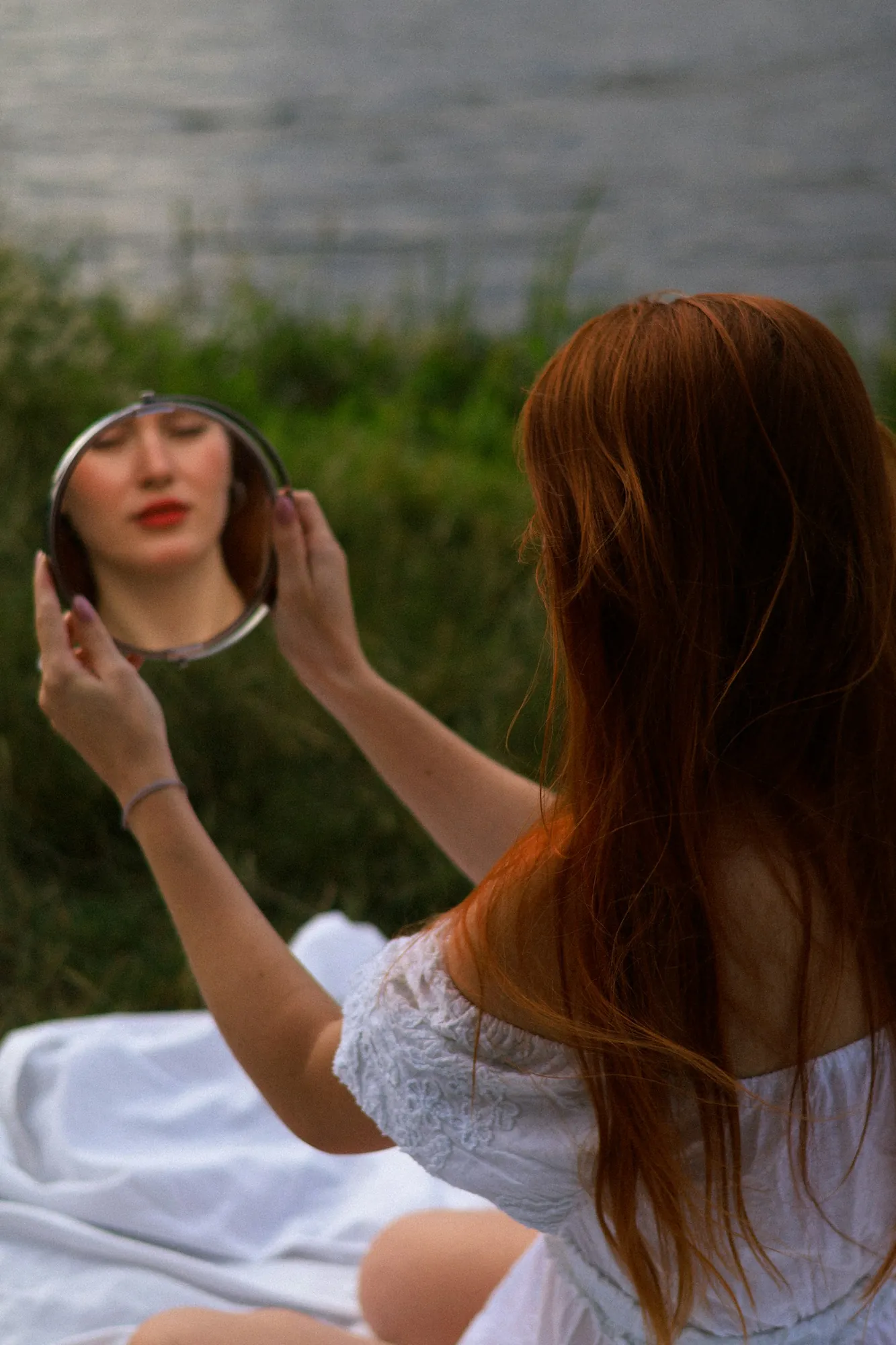 A young woman holding a round mirror up to her own face.