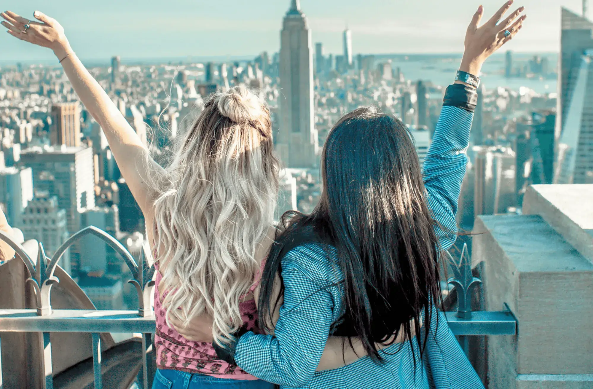Two young women on a rooftop with their arms thrown open.